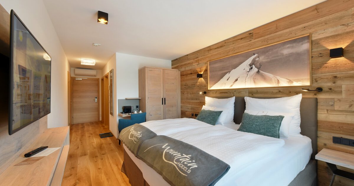 Doppelzimmer in Kaprun im Holz Stil mit einem großen Bett mit weißer Bettwäsche