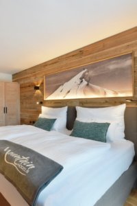 Großes Doppelbett an einer Holzwand im Berghotel in den Alpen