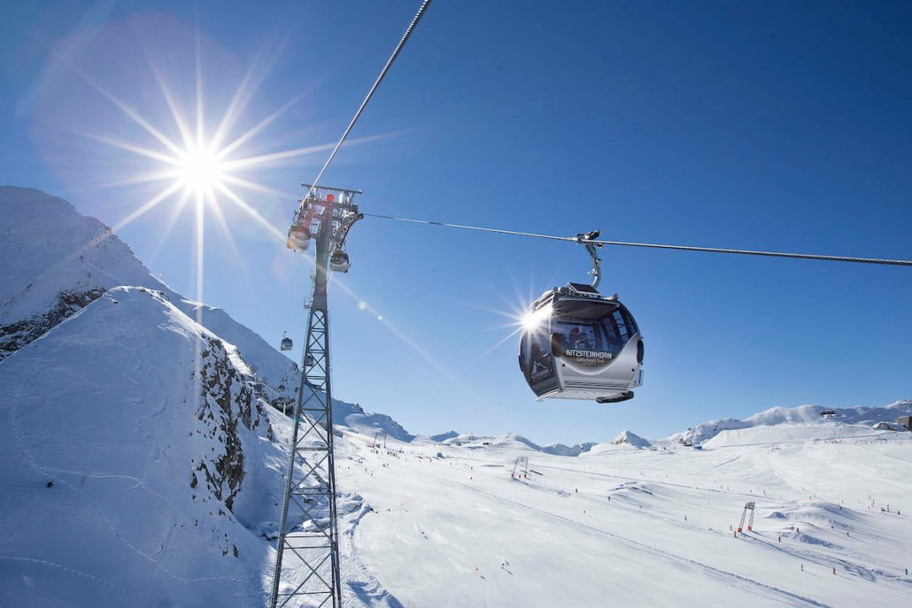 Gondelbahn vor Sonne und verschneiten Bergen.