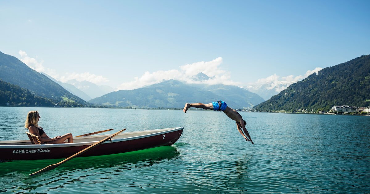 Eine Frau die im Boot auf einem See sitzt und ein Mann der gerade ins Wasser springt