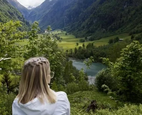 Frau die auf eine Wiese sitz und auf einen Bergsee schaut