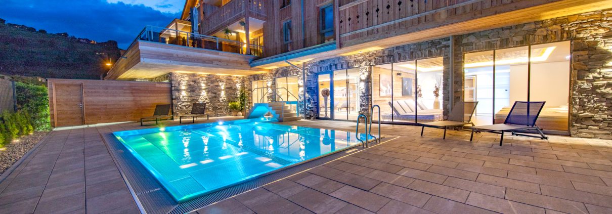 Beleuchteter Hotelpool bei Abendstimmung mit alpinem Flair